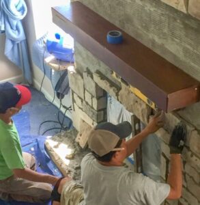 Contractors working to attach. stone veneer to a fireplace